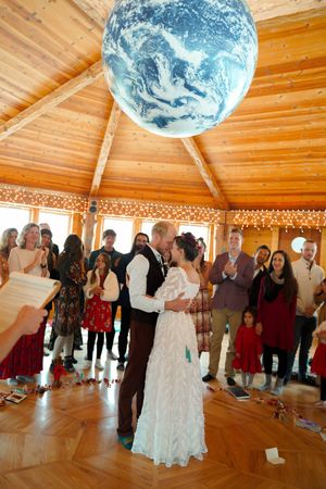 Wedding celebration under a large Earth globe installation with guests watching the couple's first dance.