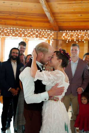 Intimate wedding moment in a wooden venue decorated with string lights as guests look on.