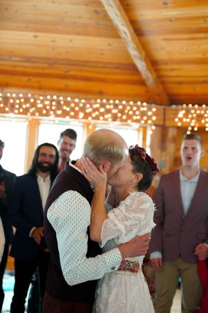 Romantic first kiss moment during wedding ceremony in wooden pavilion with string lights.