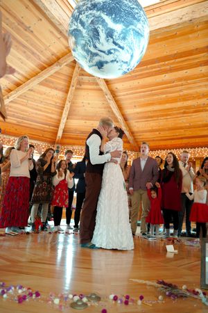 Couple shares intimate dance under large Earth globe with guests watching in circular wooden venue.