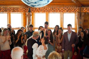 Wedding celebration with guests gathered in a warm wooden room with large windows.