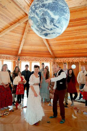 Wedding reception in wooden octagonal room featuring Earth globe ceiling fixture and string lights.