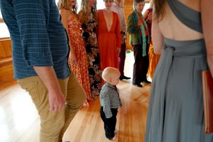 Small child walking among formal wedding guests on hardwood floor.
