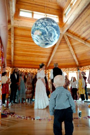 Child watching dancers under large globe decoration in wooden venue with string lights.