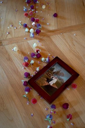 A framed photograph on wooden floor surrounded by scattered colorful paper flowers.
