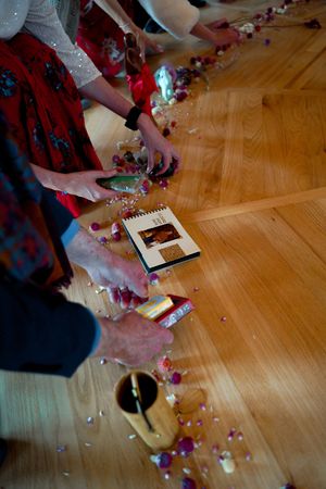 Hands arranging decorative elements and confetti on a wooden floor during an event setup.