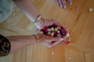 Hands gathering small colorful paper flowers on a wooden surface.