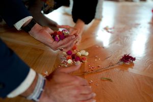 Hands arranging dried flowers and petals on a wooden surface.