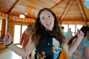A wedding guest dances joyfully in a wooden room with string lights.