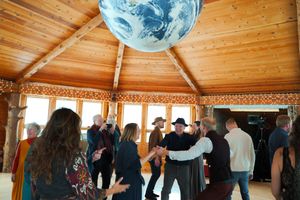 Wedding celebration with guests dancing under large Earth globe in wooden pavilion.