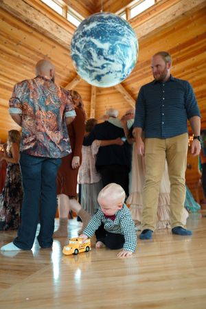 A small child plays with a toy car beneath a large Earth globe in a wooden-beamed venue.