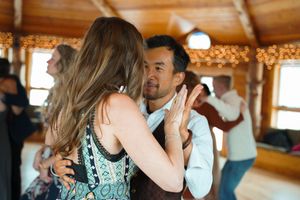 People dancing and embracing at a party in a cozy wooden lodge interior.