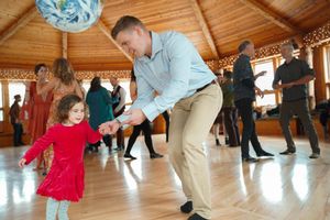 Children and adults dancing together at a wedding reception in a rustic wooden venue.