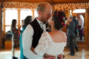 A couple shares an intimate moment during their wedding reception in a wooden room with string lights.