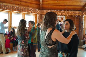 Event guests dancing together on a polished wood floor under warm lighting in a timber-frame lodge.