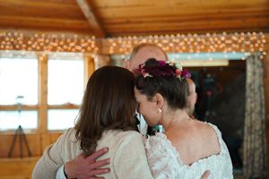 Two people embrace in a rustic venue decorated with string lights and wooden beams.