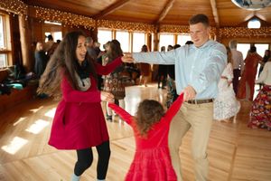People dancing and celebrating in a rustic wooden event space decorated with string lights.