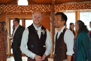 Two wedding guests share a candid moment in a rustic indoor venue decorated with twinkling lights.