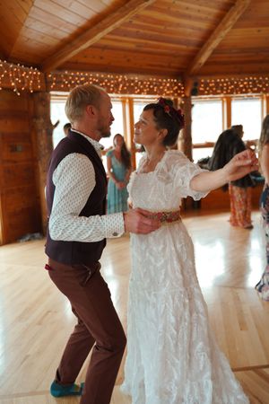 A couple dances in a rustic wooden venue decorated with string lights during a wedding celebration.