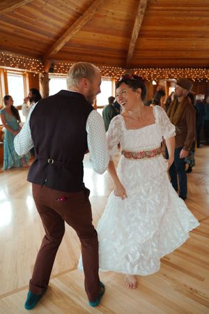 Dancing couple in a rustic venue wearing formal attire move energetically under warm lighting.