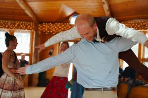 Person dancing energetically with outstretched arms in a wooden pavilion with string lights.