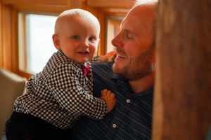Heartwarming moment between a baby in checkered shirt and adult sharing joyful laughter.