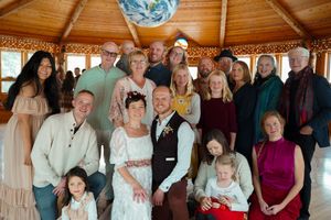 Wedding party gathers in a wooden gazebo with vaulted ceiling for a group photo.