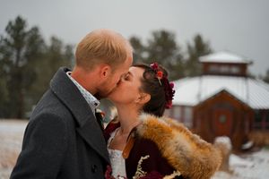 A winter wedding moment captured outside a rustic barn in the snow.