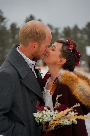 A romantic winter wedding moment with burgundy and fur accents captured against a snowy backdrop.