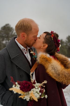 Winter wedding couple sharing a romantic kiss while holding a burgundy and white bouquet.