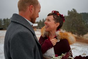 A couple shares an intimate winter moment outdoors, wearing warm coats and burgundy accessories against a snowy landscape.