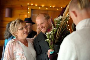 Wedding guests mingle in a warm wooden reception hall decorated with string lights.