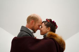 A couple embraces and shares a tender moment at a white wall.
