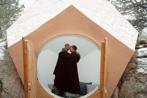 A romantic moment captured inside a rustic wooden arched dome shelter in nature.