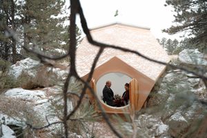 Rustic log cabin pavilion situated in a snowy winter forest setting with a peaked roof and large windows.