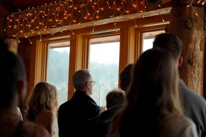 Wedding guests gather by large windows decorated with twinkling fairy lights.