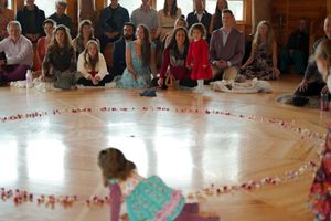 Guests seated around a circular formation of rose petals during an indoor ceremony.