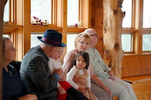 A casual gathering of people seated on wooden benches in a rustic room with large windows.