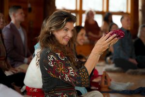 Woman in decorated clothing holds up decorative items during an indoor gathering.