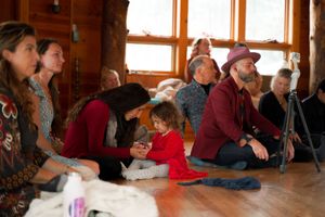 Group of people seated on floor during indoor gathering with natural lighting from windows.