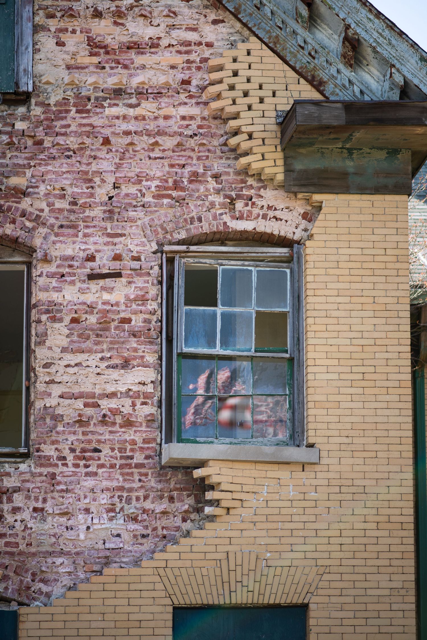 A photograph of an old brick building facade with worn yellow paint and weathered window showing urban decay in Fort Hancock, Sandy Hook, NJ