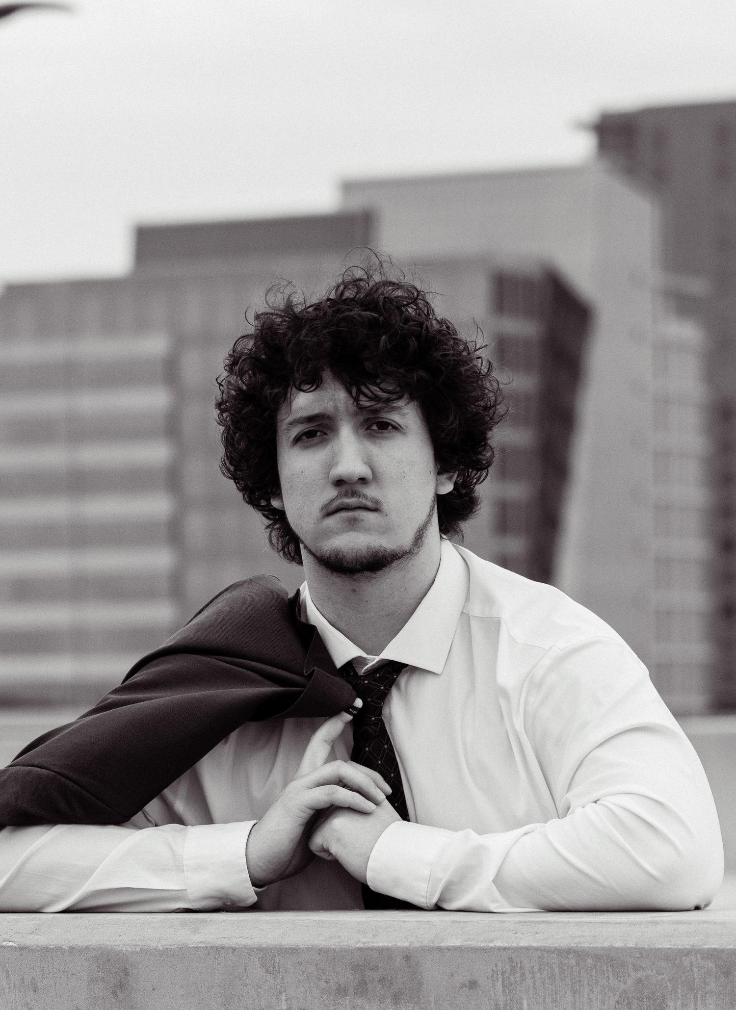 Moody black and white portrait of person in business attire against urban backdrop.