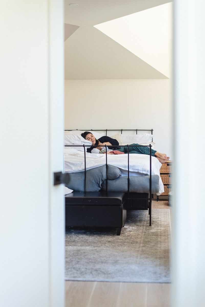 View through doorway of person lying casually on bed in modern minimalist bedroom.