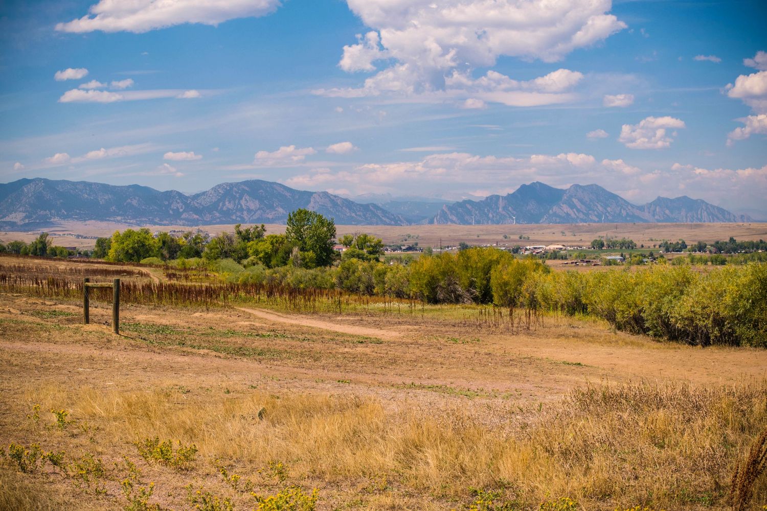 Rolling hills and mountains frame a rural landscape with scattered trees under blue skies.