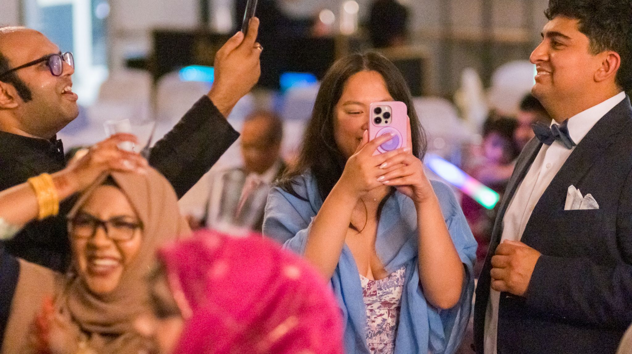 Guests taking photos with phones at a celebratory event with colorful decorations.