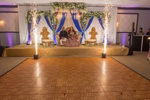 Elegant wedding stage setup with blue drapes, floral decor, and wooden dance floor.