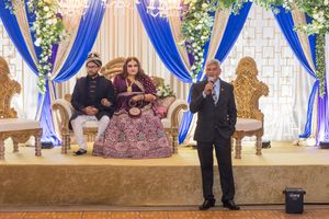 Wedding reception setup with ornate throne chairs and blue drapery decorations.