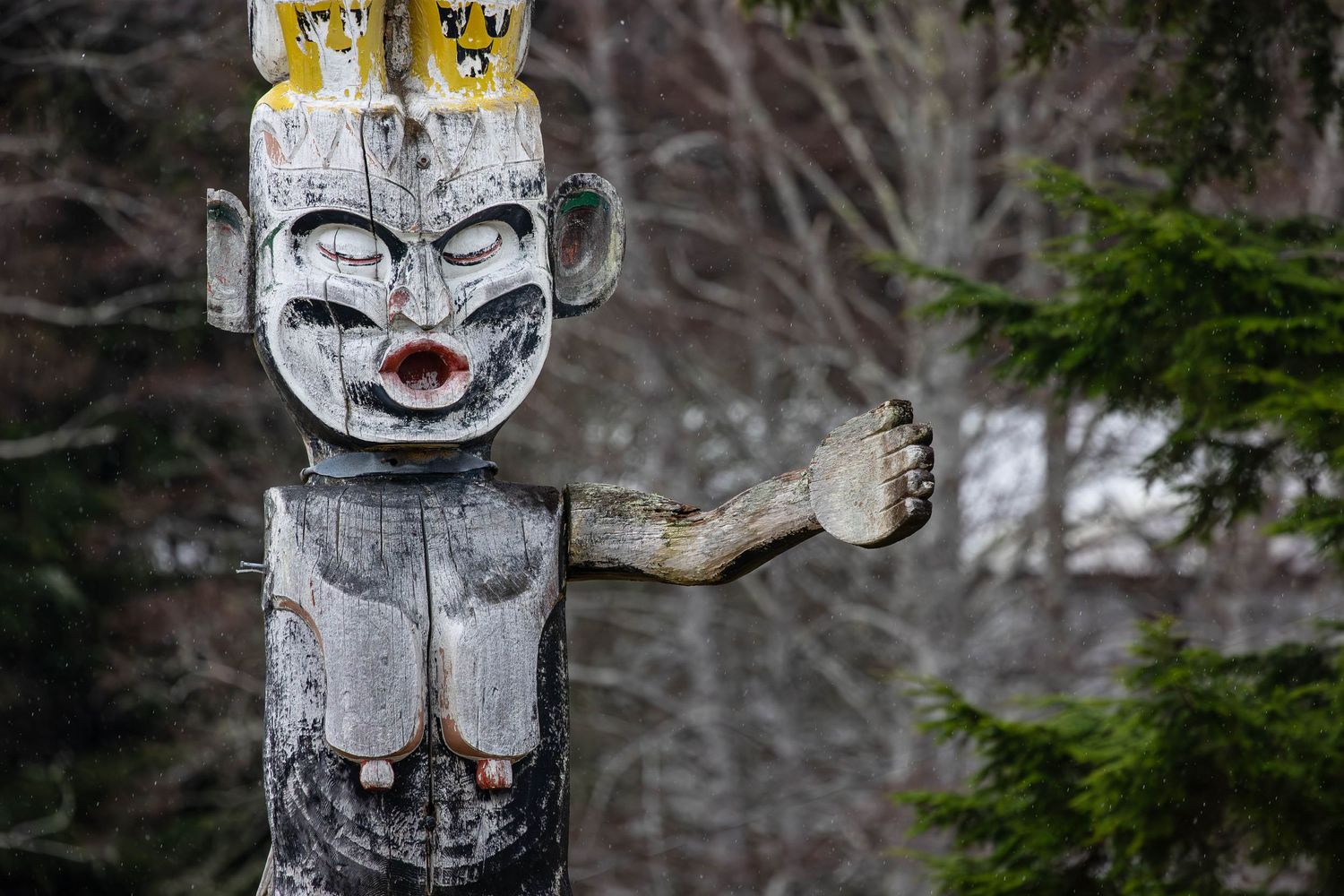 Traditional Native American totem pole with white crown and face carved into weathered wood.