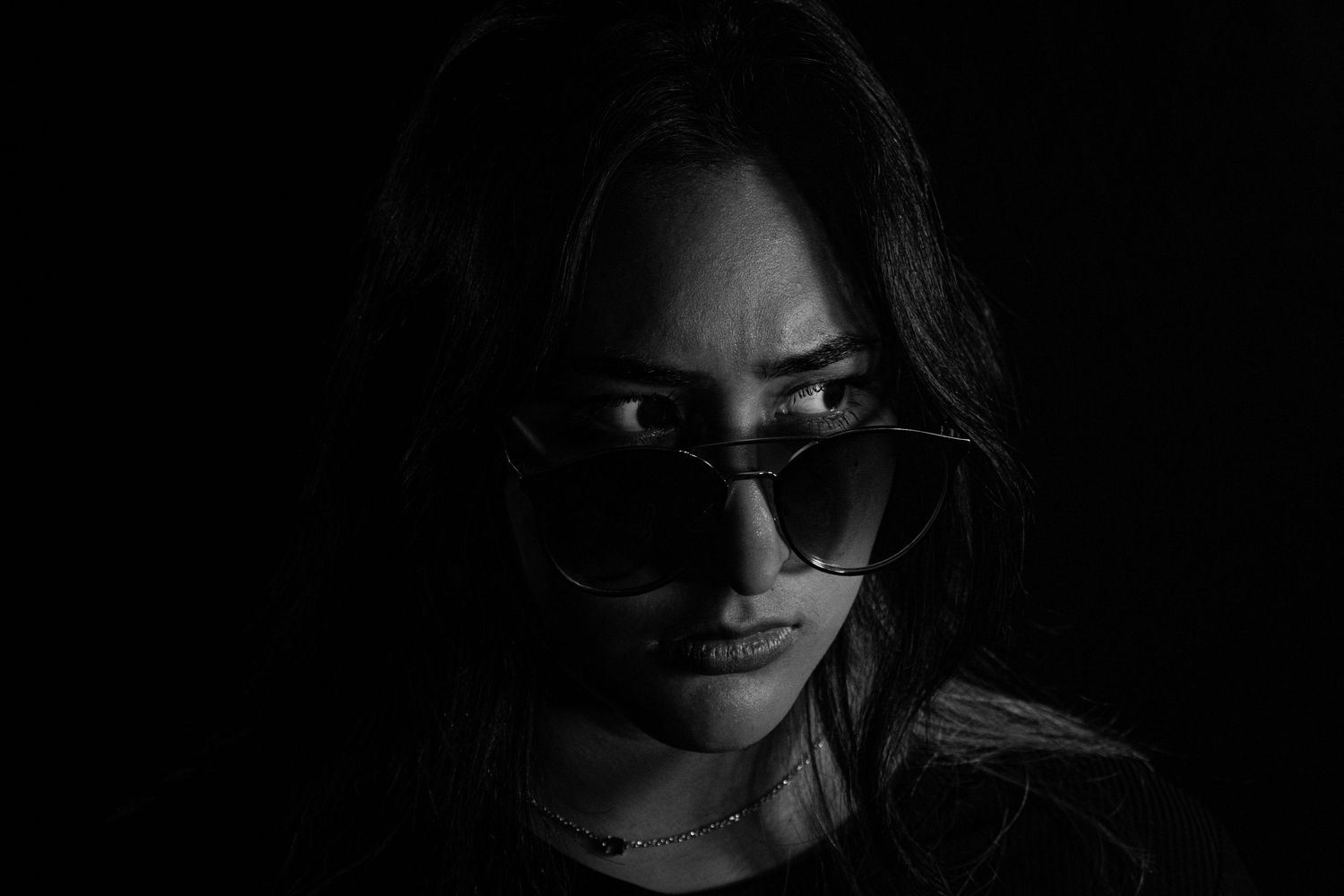 Dramatic black and white portrait showing silhouette with sunglasses against dark background.