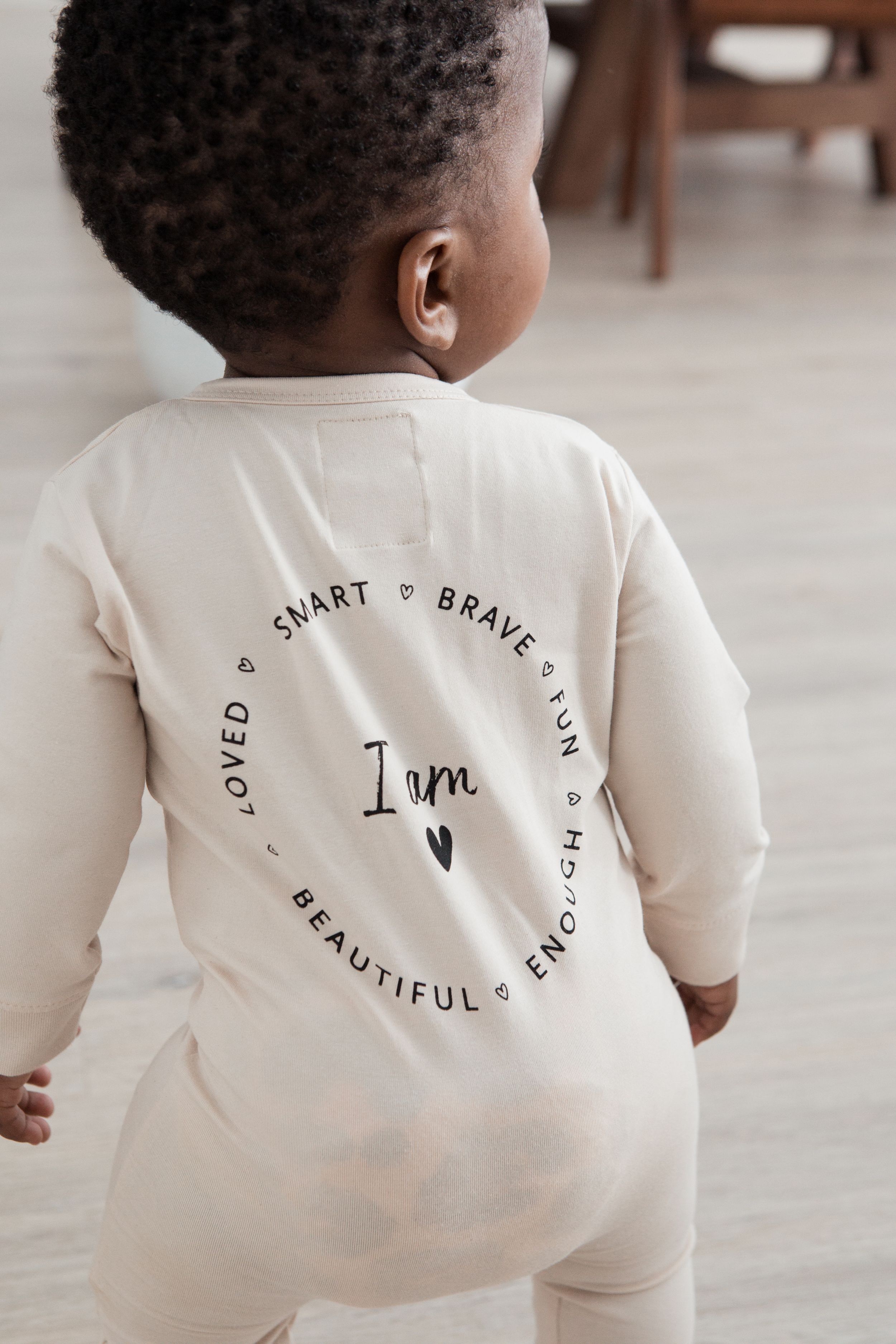 Back view of cream-colored onesie with inspirational text circle design.